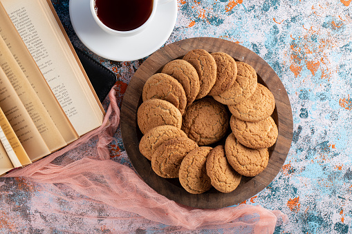 Top view of snack table. Cookie on wooden tray with book and cup of tea. High quality photo