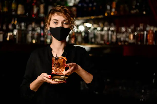 Photo of view of woman in black mask and holding glass with cocktail