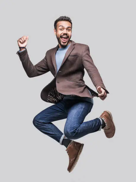 Excited laughing young man is jumping, isolated on grey background