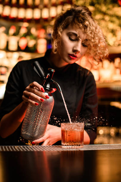 istock attractive female bartender stands behind the bar and accurate pours drink from siphon into glass 1304522937