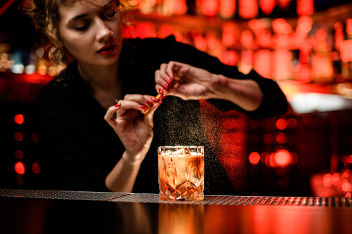 mujer camarero espolvorea suavemente en vidrio con cóctel alcohólico frío en el mostrador del bar photo