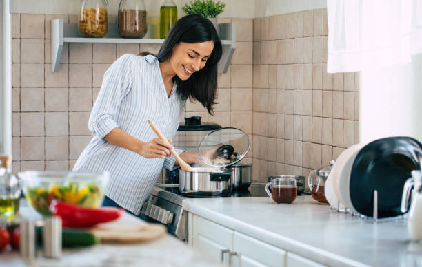 beautiful happy young woman is cooking in the home kitchen and testing some soup from the pan on the stove - eating female healthcare and medicine healthy lifestyle imagens e fotografias de stock