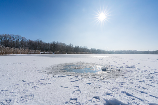 The picture shows the lake in winter. The surface of the water in the lake froze, forming an interesting pattern.