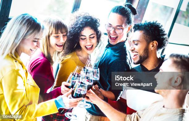 Young Multiracial People Drinking And Toasting Red Wine At Dinner Party Happy Drunk Friends Having Fun Together At Restaurant Winery Bar Dinning Lifestyle Concept On Bright Vivid Backlight Filter Stock Photo - Download Image Now