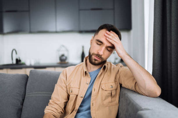 istock Tired caucasian bearded man sits on the sofa, having a headache. Unhealthy guy catch a cold or having flu, upset about illness, unhappy man feel depressed 1304528356