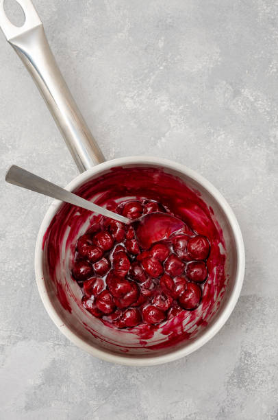 istock Cherry cooked with sugar and starch in a saucepan to make chocolate roll cake Black forest on a gray concrete background. Recipe step by step. Top view. 1304528397