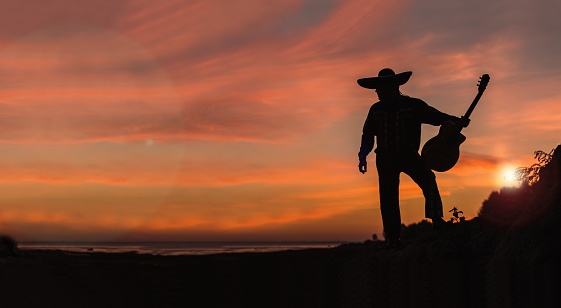 Silhouette of a Mexican musician with a guitar. Mariachi on the beach at sunset.