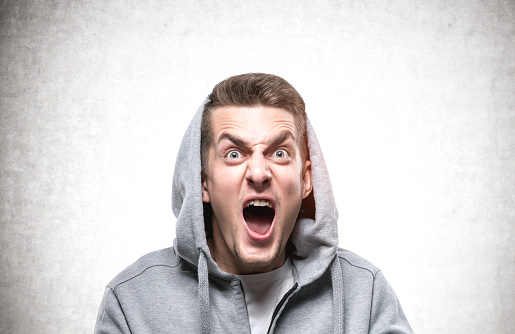 Portrait of shouting young European man in gray hoodie. Concept of anger management and strong emotions