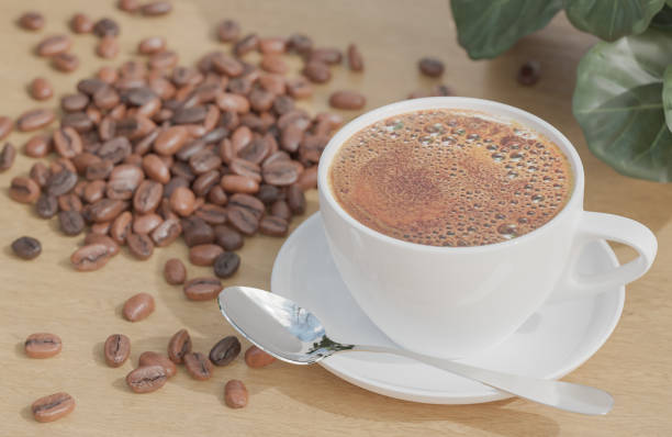 istock White Coffee cup and coffee beans on wood table with plant and white brick wall background. 1304535080