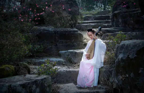 A woman in ancient costume sits under a red plum tree playing a Chinese guqin