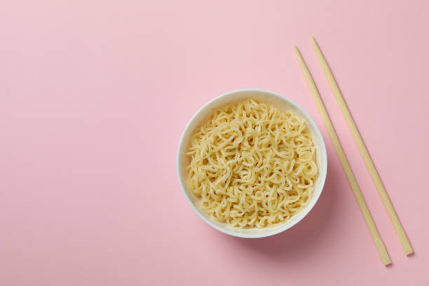 istock Bowl with noodles and chopsticks on pink background 1304536135
