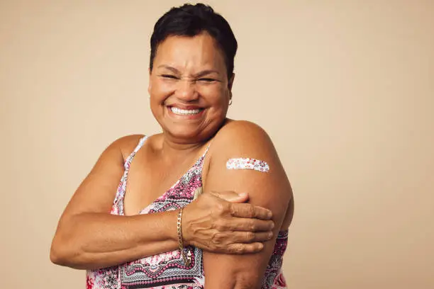 Portrait of a smiling senior woman receiving a vaccine. Mature woman showing her arm with bandage after vaccination.
