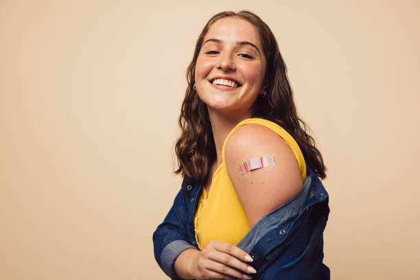 I have taken the vaccine Portrait of a female smiling after getting a vaccine. Woman holding down her shirt sleeve and showing her arm with bandage after receiving vaccination. vaccination stock pictures, royalty-free photos & images