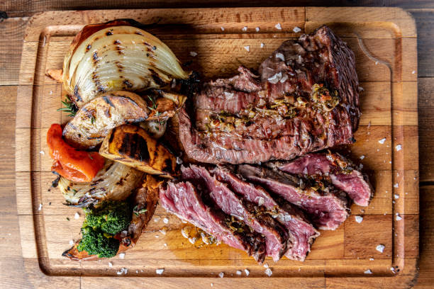 argentinischer fleischschnitt namens vacio mit gemüse und serviert auf einem holzbrett. - chimichurri horizontal beef steak stock-fotos und bilder