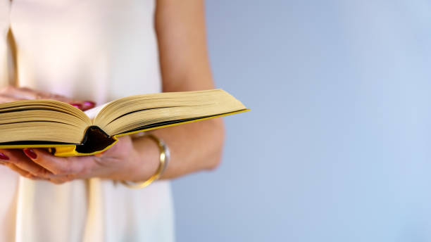 istock Woman holding a book and reading in standing posture on blue background with copy space. Concept, reading. 1304542170