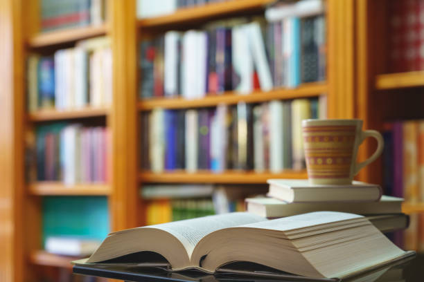 istock library with many books to read, arranged on shelves. Open book and cup close-up. Copy space. 1304542198