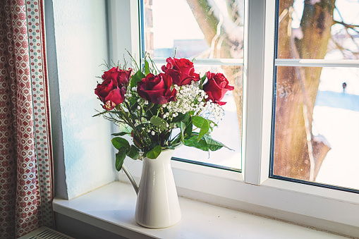 Vase of fresh red roses at the bright window