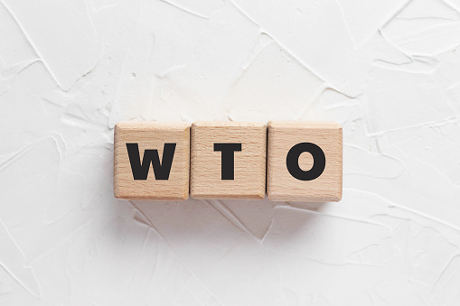 Text WTO on wooden cubes on white textured putty background. Abbreviation of 'World Trade Organization'. Square wood blocks. Top view, flat lay.