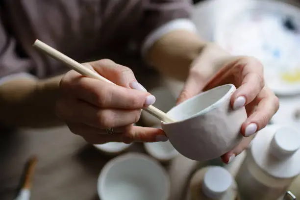 The process of hand-painting a ceramic hand-made bowl. Emphasis on the beautiful female hands of the artist.