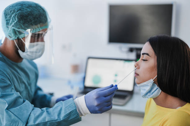 istock Medical man working with protective equipment performs coronavirus nose swab on young woman patient - Covid-19 PCR test 1304551994