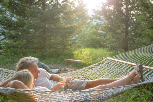 Mature couple relaxes in hammock in backyard, sunset They are sharing a glass of wine hammock relaxation women front or back yard stock pictures, royalty-free photos & images