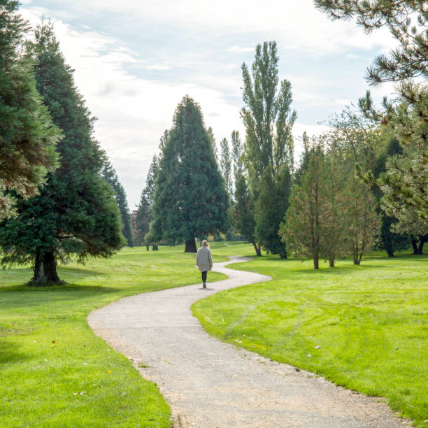 donna cammina attraverso parco urbano su sentiero - landscaped spring canada footpath foto e immagini stock