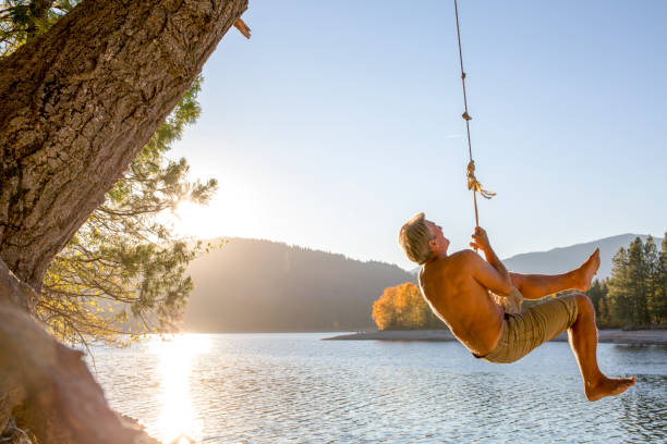 homem balança em uma corda sobre um lago ao amanhecer - self reflection - fotografias e filmes do acervo