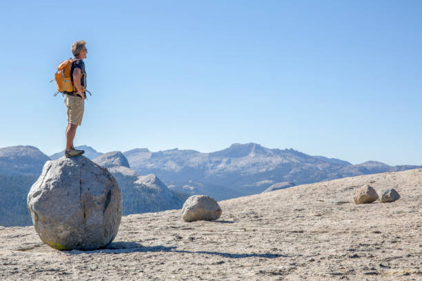 Hiker balances on a rock boulder above mountains