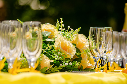 The bride's bouquet of roses lies on a yellow table between champagne flutes. Wedding ceremony.