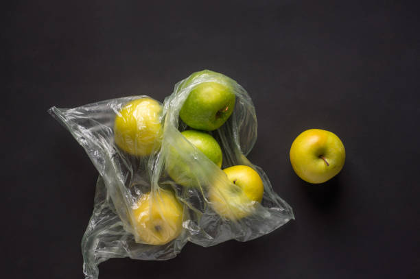 istock single use plastic packaging issue. green apples in plastic bags  on a dark background 1304558297