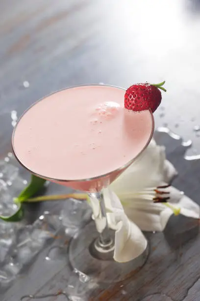 Photo of Velvet Socks cocktail mixed with tequila, milk, grenadine, ice and garnished with a strawberry and a large white flower.