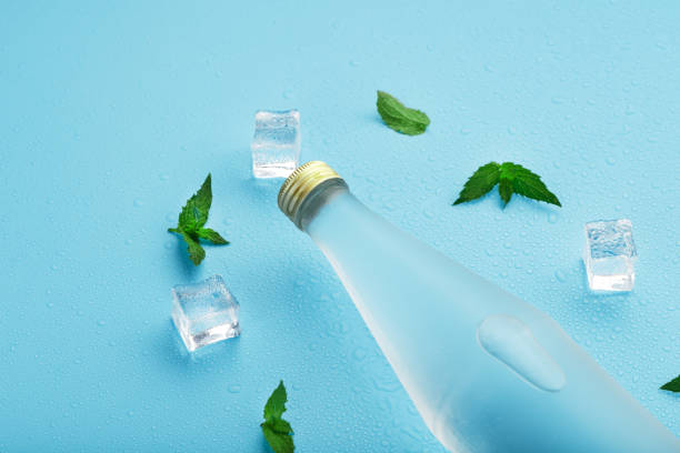 istock Bottle with an ice cold beverage, ice cubes, drops and mint leaves on a blue background. 1304560730