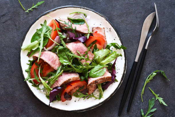 istock Mix salad with tomatoes and medium beef in a plate on a dark background. 1304561397