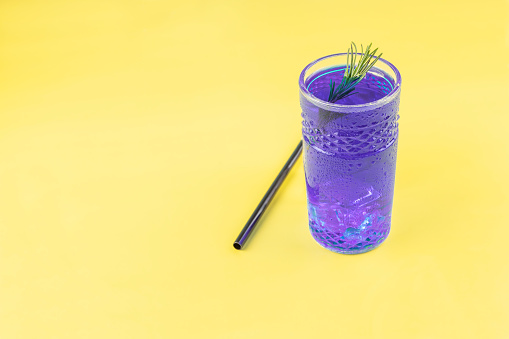thai blue iced tea with a sprig of rosemary in a glass on a yellow background
