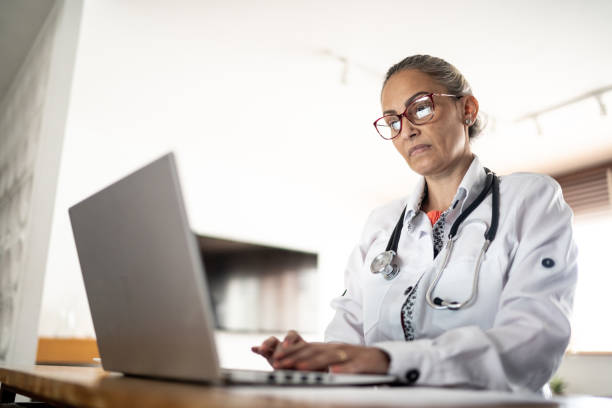 Mature doctor working using laptop at home