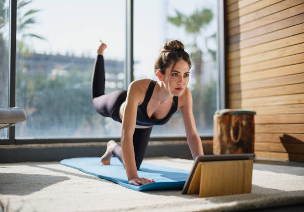 verticale d’une belle formation de femme à la maison et observant des leçons en ligne dans la tablette numérique - home fitness photos et images de collection