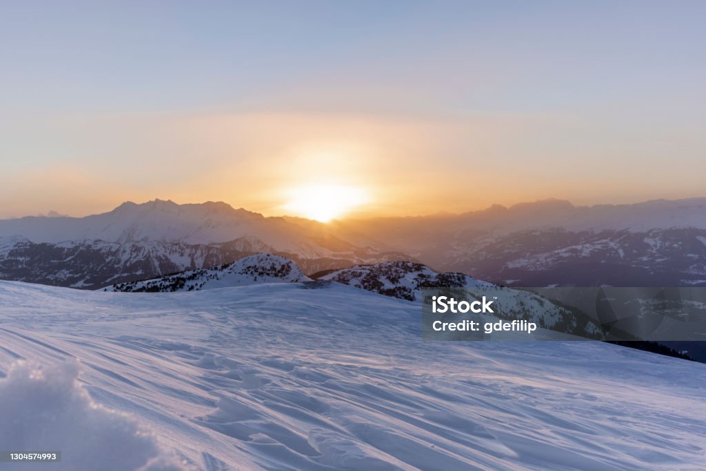The sunset in winter during a wind storm with the snow being blown away on a peak near Lenzerheide in Switzerland Arosa Stock Photo
