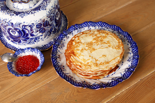 Traditional Russian Crepes Blini stacked in a plate with red caviar, on a wooden table. Russian festive meal Maslenitsa or Maslenitsa. Gzhel tableware.