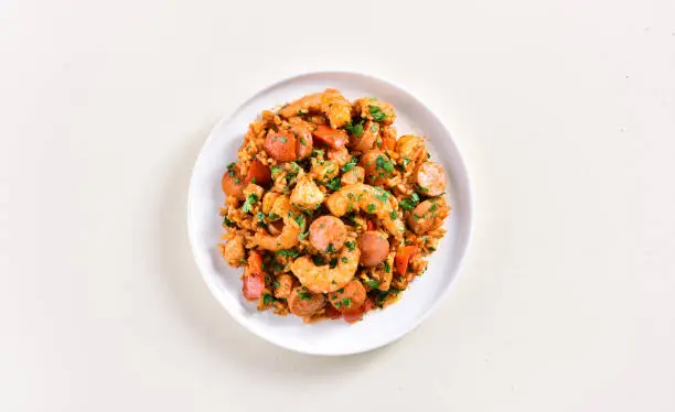 Creole jambalaya with prawn, chicken meat, smoked sausages and vegetables on plate over light background. Top view, flat lay, close up