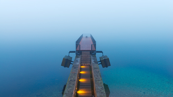 Long exposure of the bridge in calm, turquoise, smooth water and morning fog over the lake. the La Passerelle de l'Utopie bridge near street quai Ostervald. 02/06/2021 Neuchâtel, canton neuchatel, Switzerland