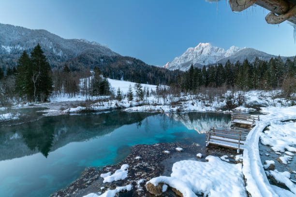 istock romantic path through the snow along a beautiful emerald, clear volcanic lake in winter at a touristic nature reserve in the Alps. Reflection of snowcapped mountains glowing in the rising sun. 1304586417