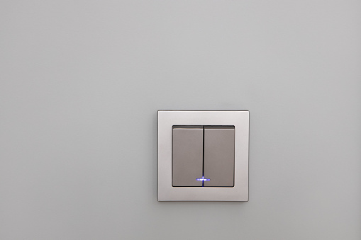 Fashionable modern silver light switches on a gray wall, opposite view. Switch with night illumination. Concept interior details, electrical equipment, device. Horizontal.