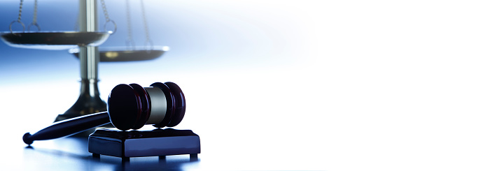 A gavel rests in front of a justice scale on a blue background that provides ample room for copy and text.