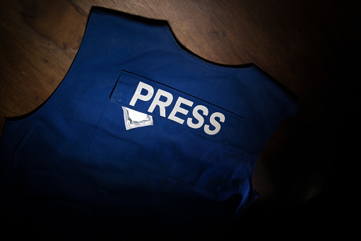 Media Journalism fake news concept. Blue journalist (press) vest in dark with backlight and fog. Dirty money on journalist vest. Selective focus