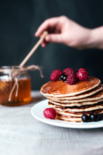 istock Pancakes with berries and honey on white plate, hand holding spoon in jar 1304597680