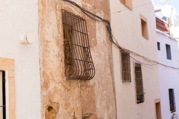 Old wall with peeling paint, scratched vintage plaster and windows with rusty iron forged grate.