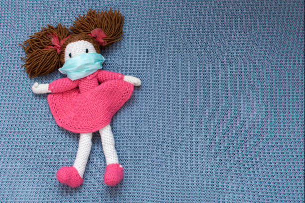 Knitted doll with protective medical mask background with copy space. Quarantine during World Pandemic of Coronavirus Covid-19 concept. Stay at home, stay safe.