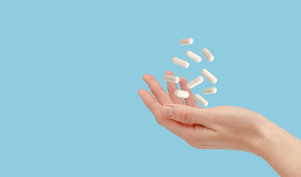 píldoras blancas flotando sobre la mano femenina aislada en azul. concepto de salud y tratamiento. copiar espacio - vitamin e capsule medicine pill fotografías e imágenes de stock