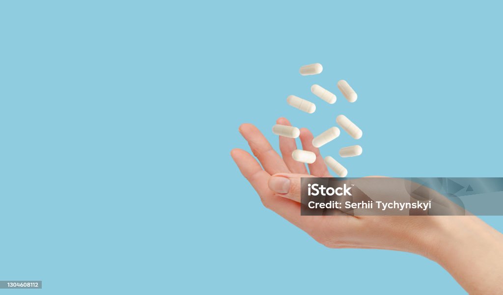 White pills floating over female hand isolated on blue. Healthcare and treatment concept. Copy space Medicine Stock Photo