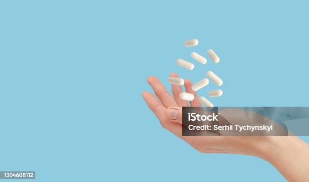 White Pills Floating Over Female Hand Isolated On Blue Healthcare And Treatment Concept Copy Space Stock Photo - Download Image Now